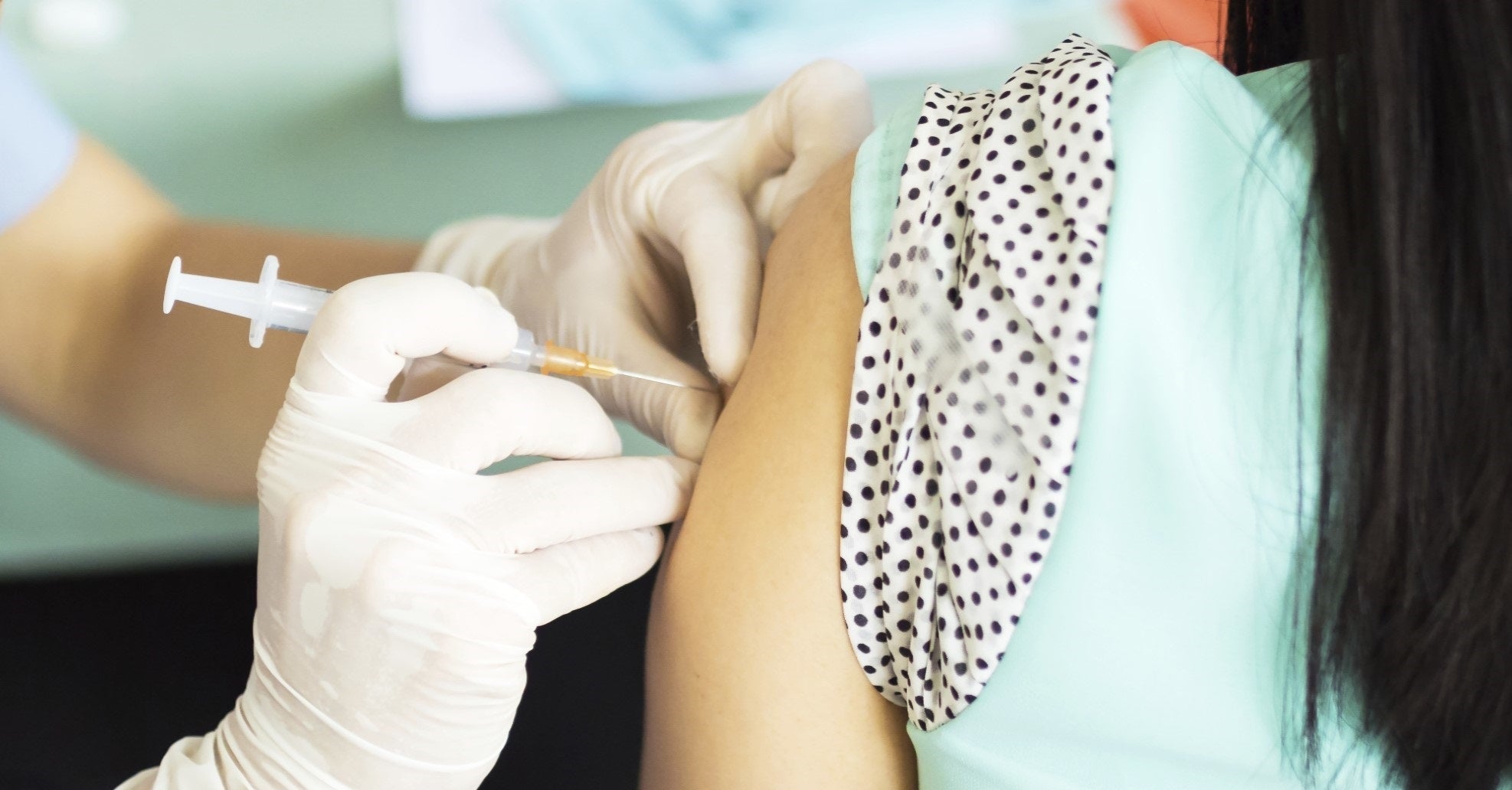 A gloved pharmacist giving a vaccination into the upper arm of a seated patient